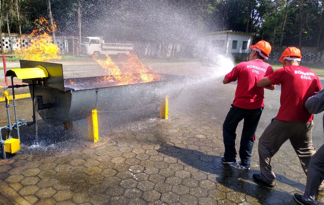 Dois bombeiros civis controlando a linha de mangueira sobre bandeja em chamas